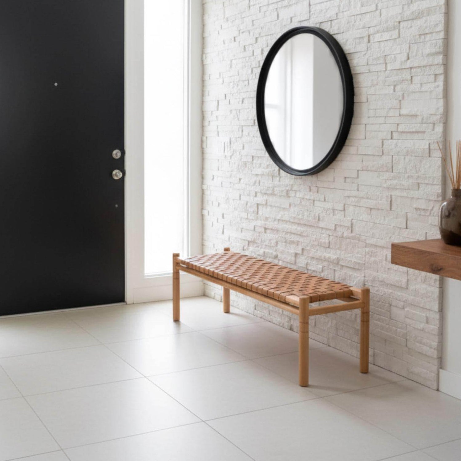 Modern interior with a black door, wooden bench, and round mirror on a white brick wall.