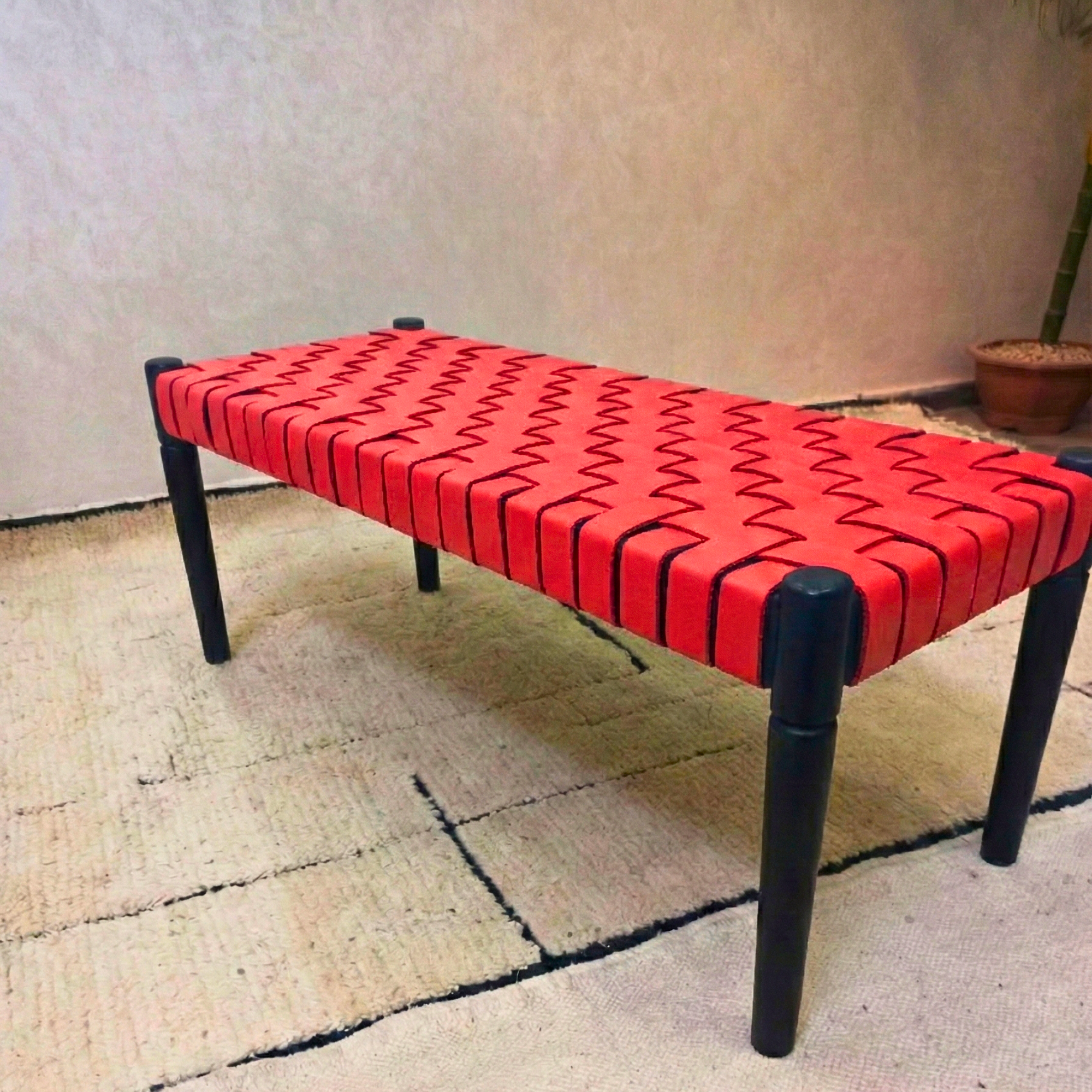 Red woven bench with black legs on a textured floor