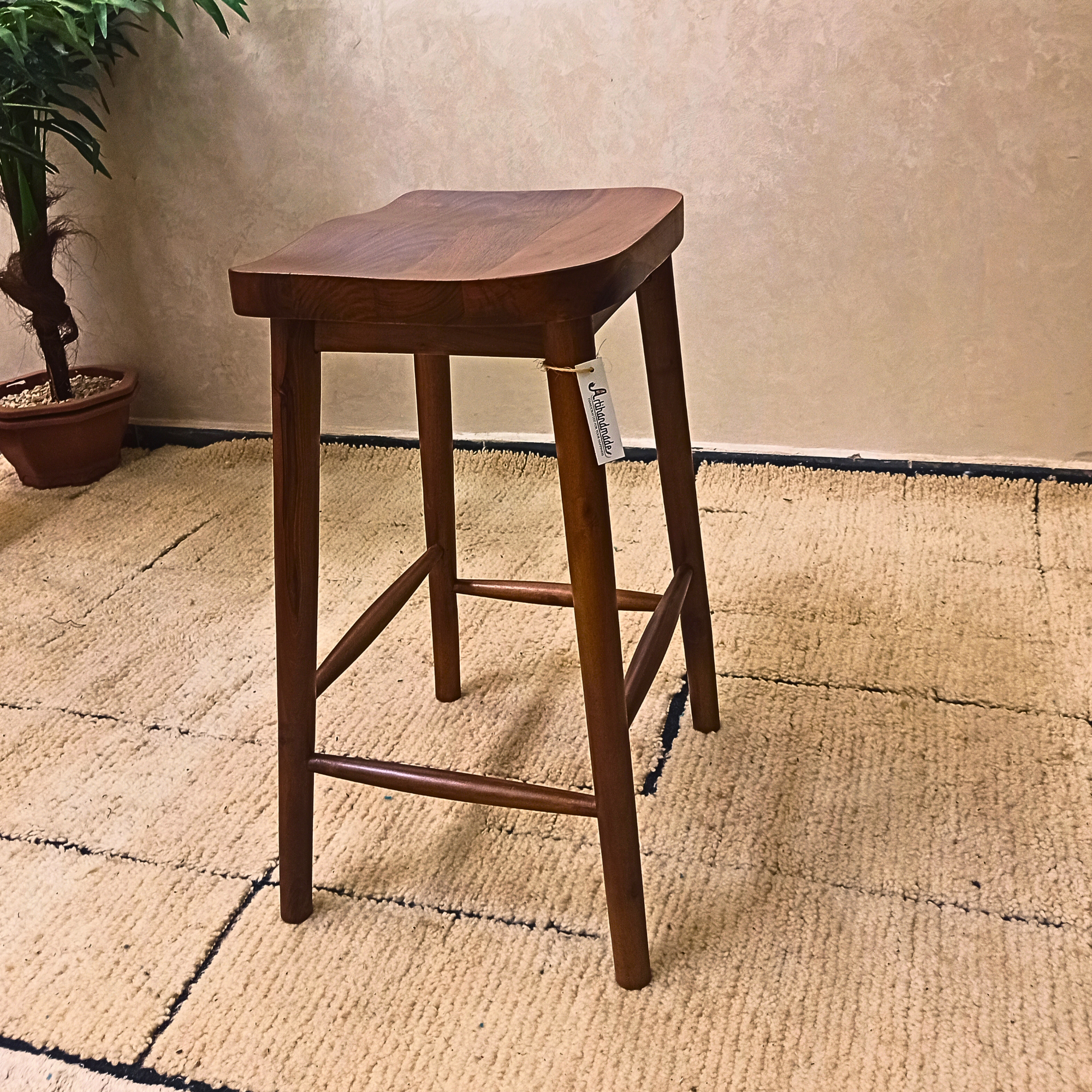 Wooden bar stool on a textured floor with a plant in the background