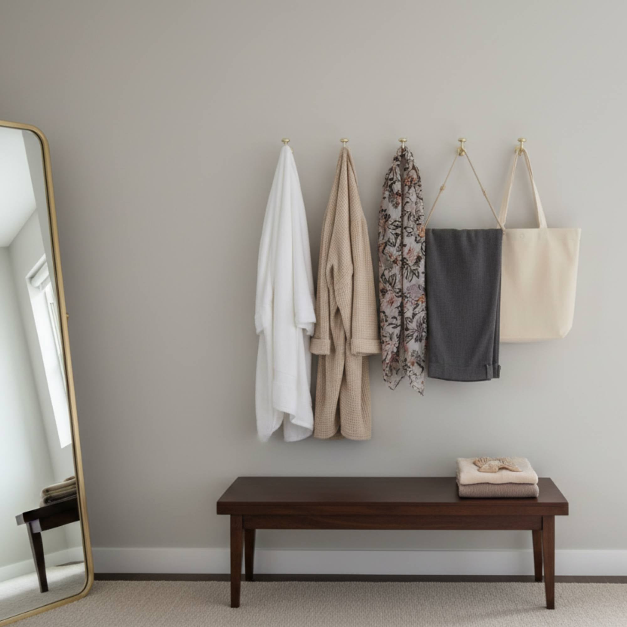 Hanging clothes and a bench in a room with a large mirror.