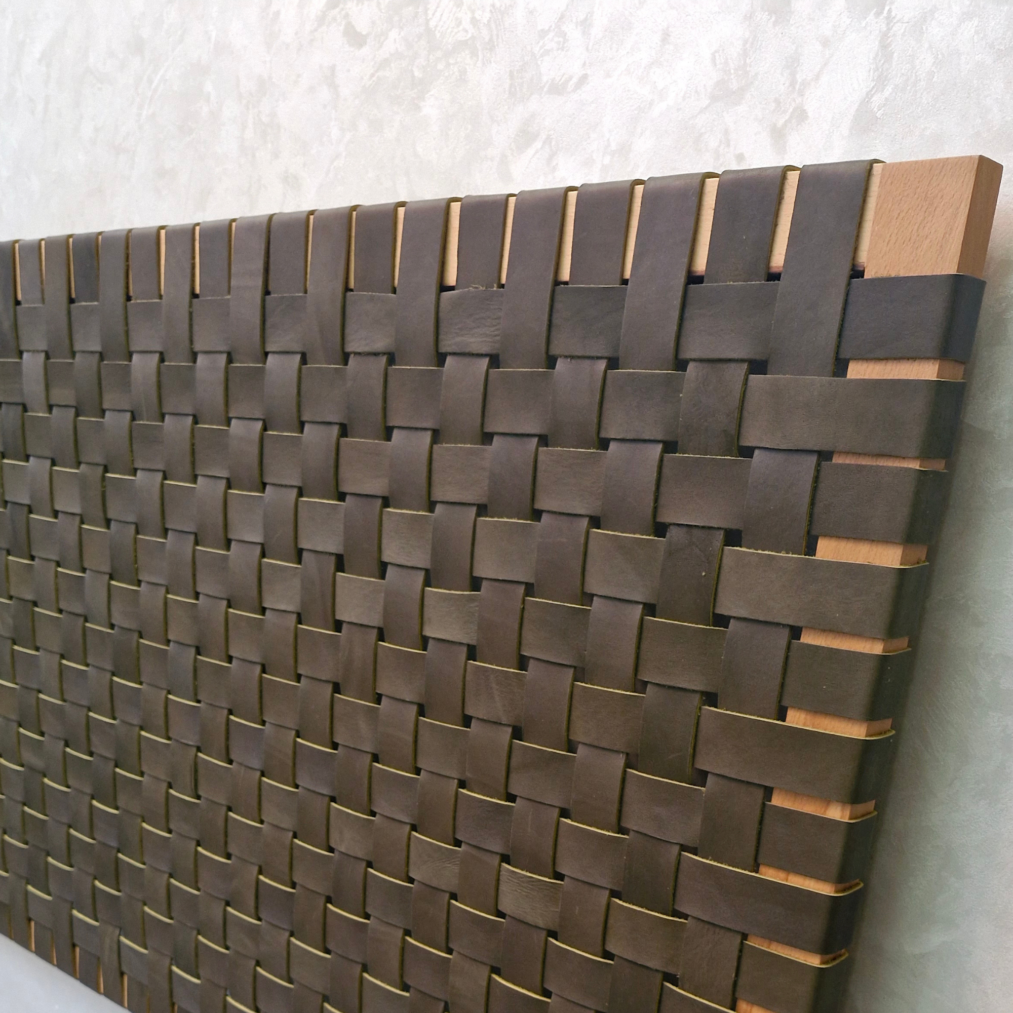Woven wooden panel with a basketweave pattern on a textured wall.