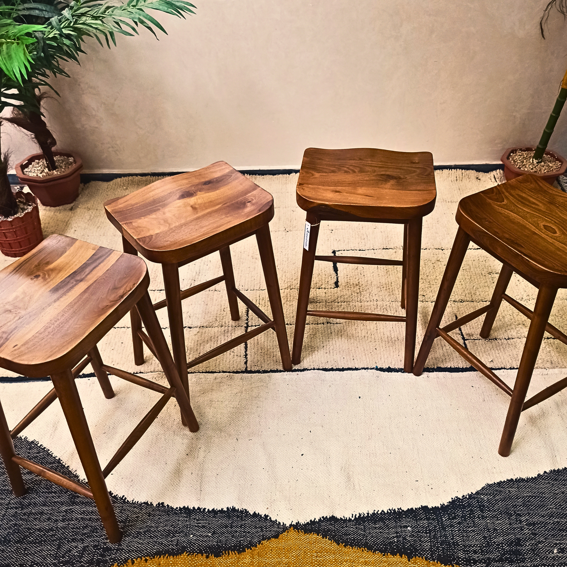 Set of walnut wooden stools in a room with a rug and plants.