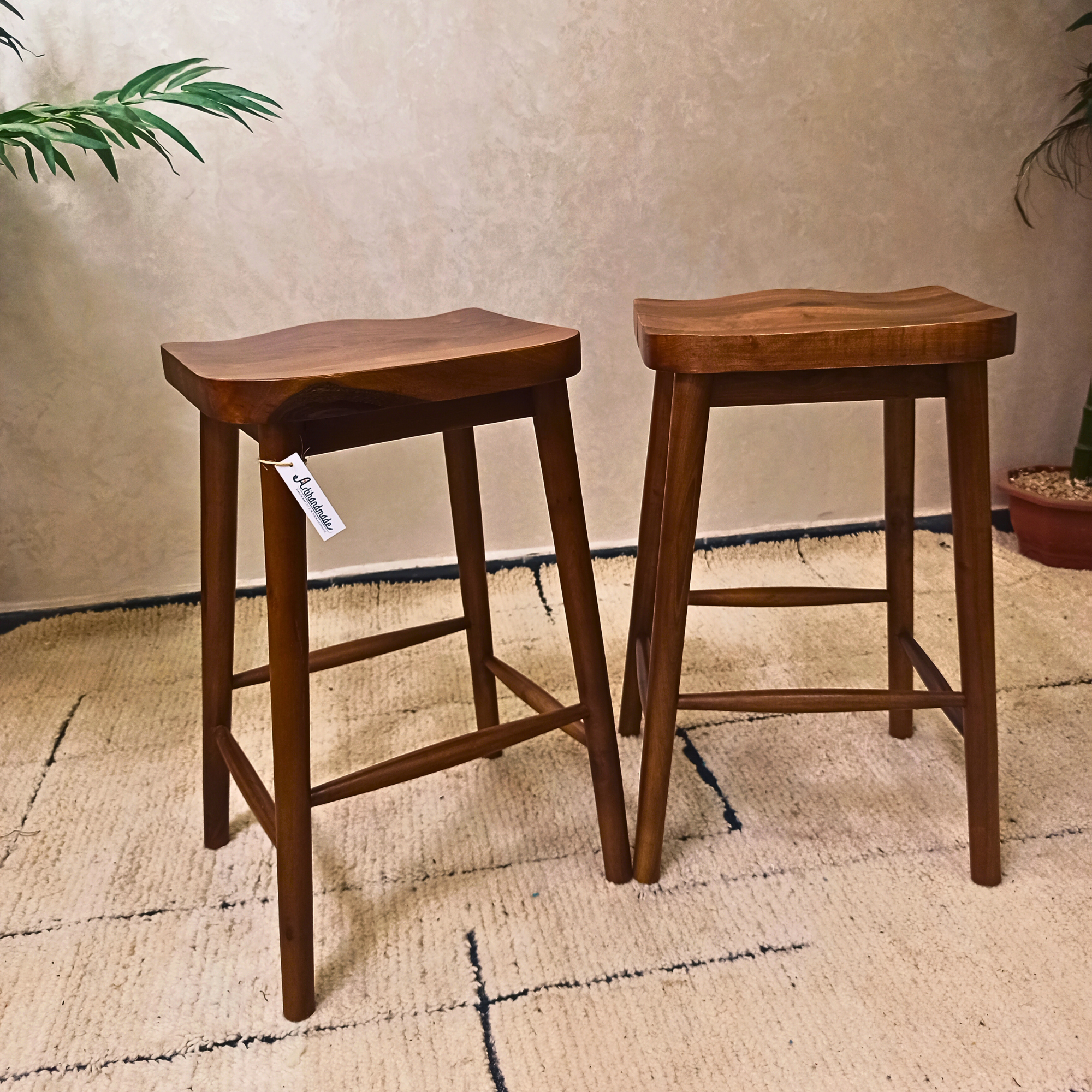 Two wooden bar stools on a textured rug with a neutral wall background.