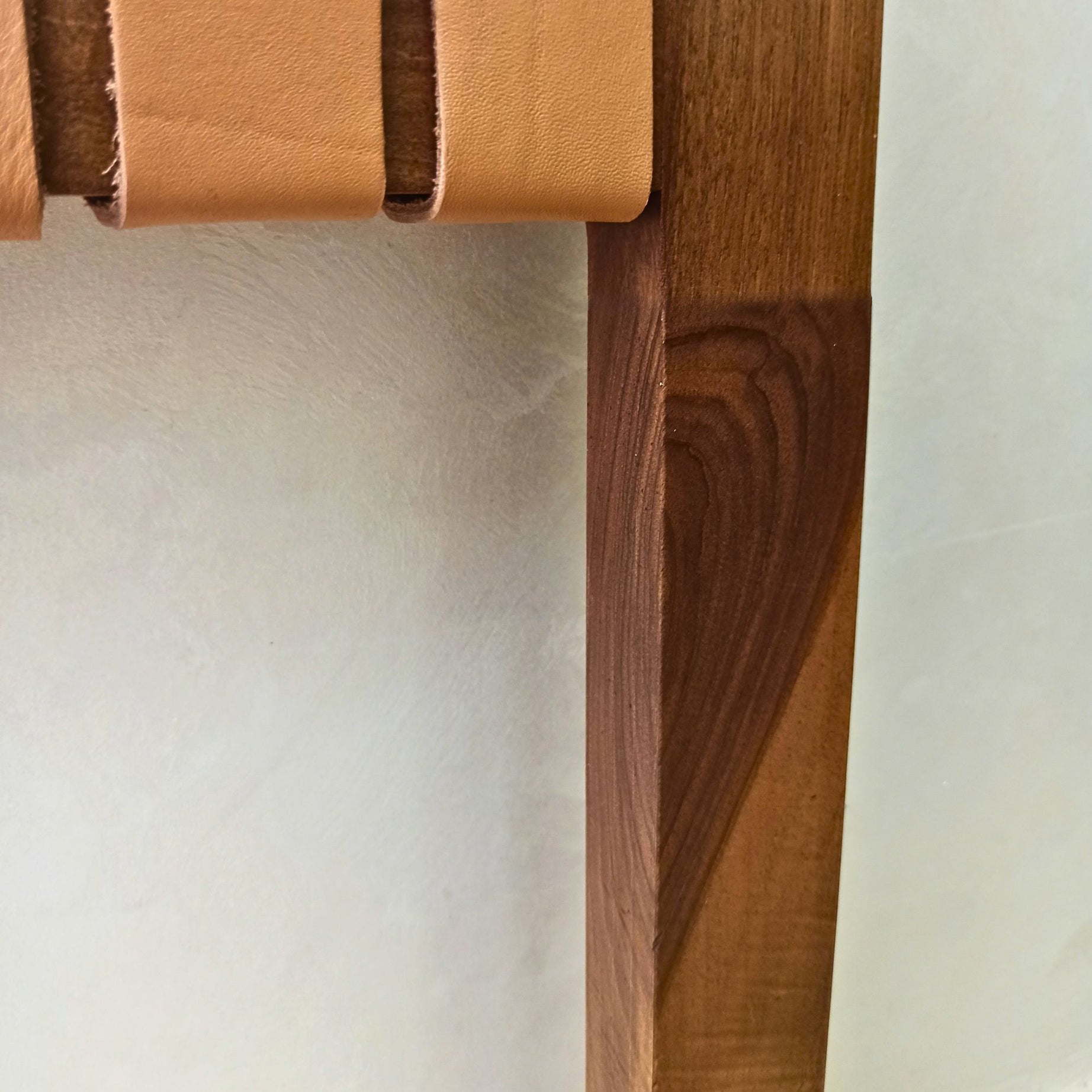 Close-up of a walnut wood shelf with a leather strap on a light background